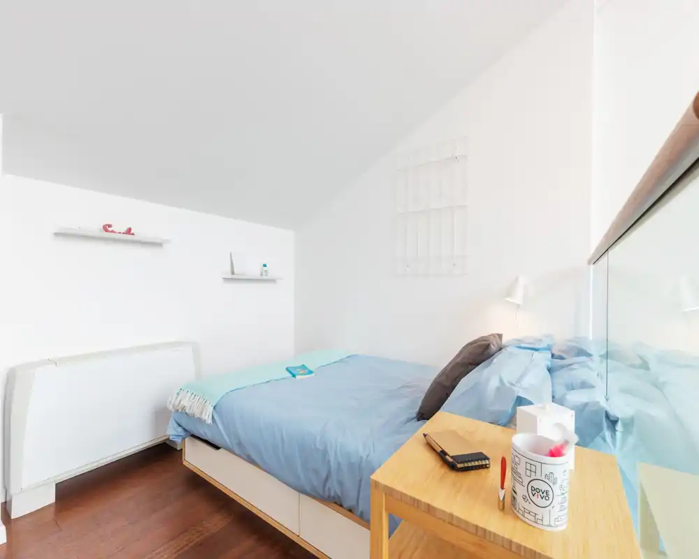 Cozy, bright bedroom with a neatly made double bed, bedside table and modern minimal décor. Natural light and soft tones create a calm atmosphere, ideal for rental listings.
