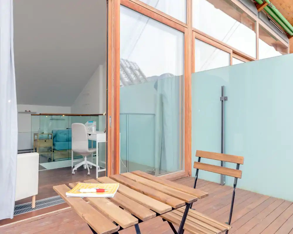 Sunny wooden terrace with a small bistro table and chairs opening onto an interior room—ideal for morning coffee and fresh air.