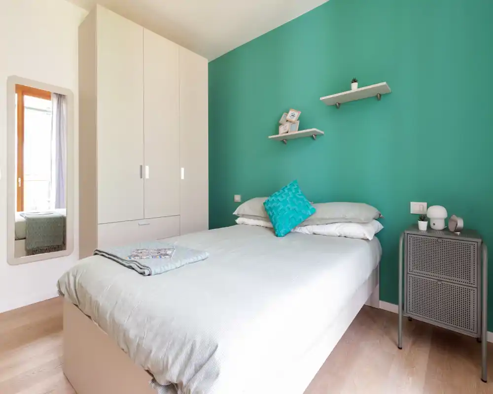 Bright, modern bedroom with a teal accent wall, double bed neatly made, bedside table and wardrobe — ideal for a clean, calm rental listing.