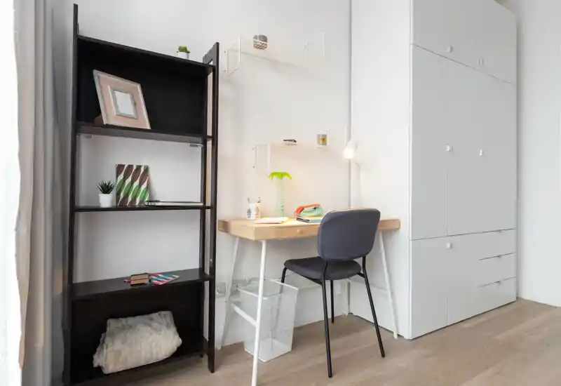 Bright, minimal bedroom corner with a compact wooden desk, upholstered chair and built-in white wardrobe — ideal for a small home office or study nook.
