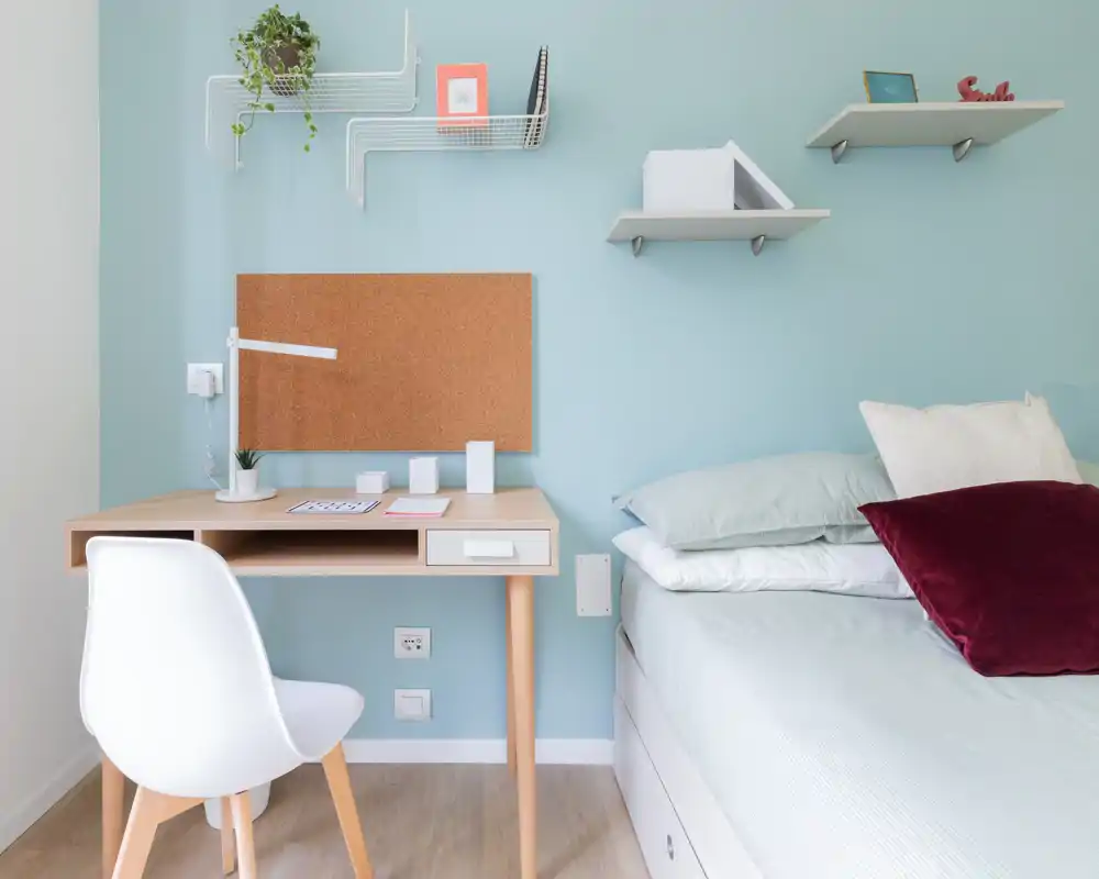 Bright, neatly staged small bedroom with a work desk and a comfortable bed dressed in soft linens and decorative pillows — ideal for single occupancy or a student flat.