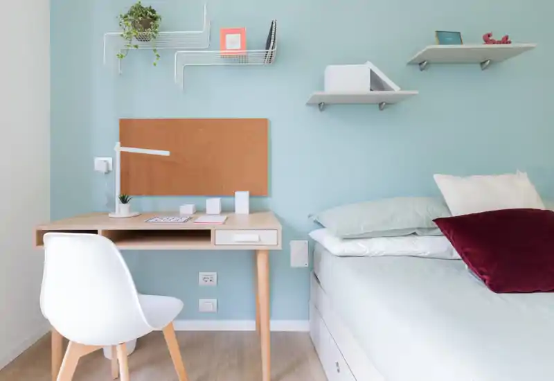Bright, neatly staged small bedroom with a work desk and a comfortable bed dressed in soft linens and decorative pillows — ideal for single occupancy or a student flat.