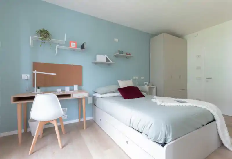 Bright, modern single bedroom with a neatly made bed, built-in storage drawers, a compact desk and soft pastel walls — ideal for a student or single occupant.