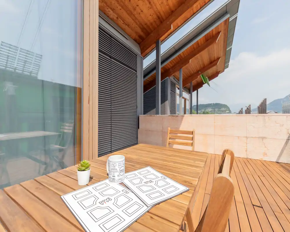 Terrasse en bois ensoleillée avec table et chaises, une petite plante et une tasse — idéale pour se détendre en plein air avec vue sur les collines.