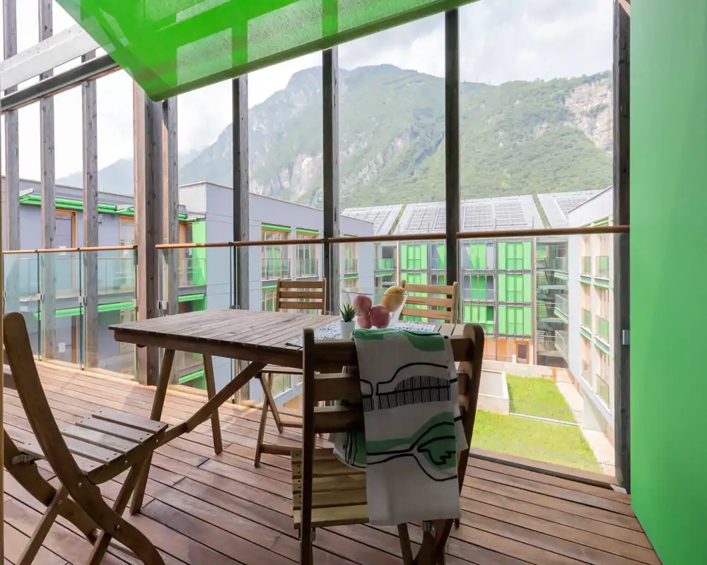 Sunny wooden balcony with a dining table and chairs, glass balustrade and mountain views — ideal for outdoor meals and relaxation.