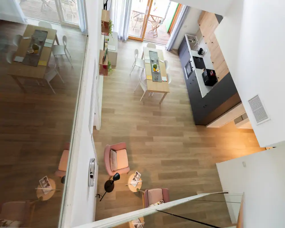 Bright, modern open-plan living area with a compact dining table and a kitchenette; cozy seating and large glass doors opening to a balcony provide natural light and a welcoming atmosphere.