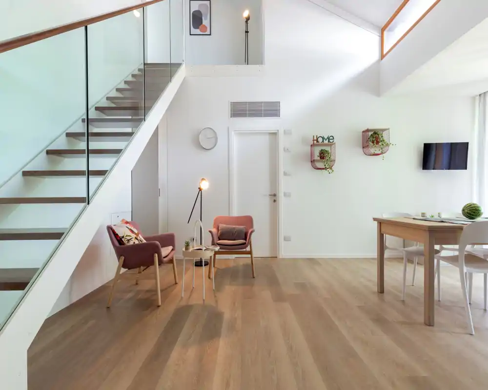 Bright, modern living area with high ceilings, contemporary armchairs, a floor lamp and a dining table — an airy, well-styled open-plan space ideal for relaxation.