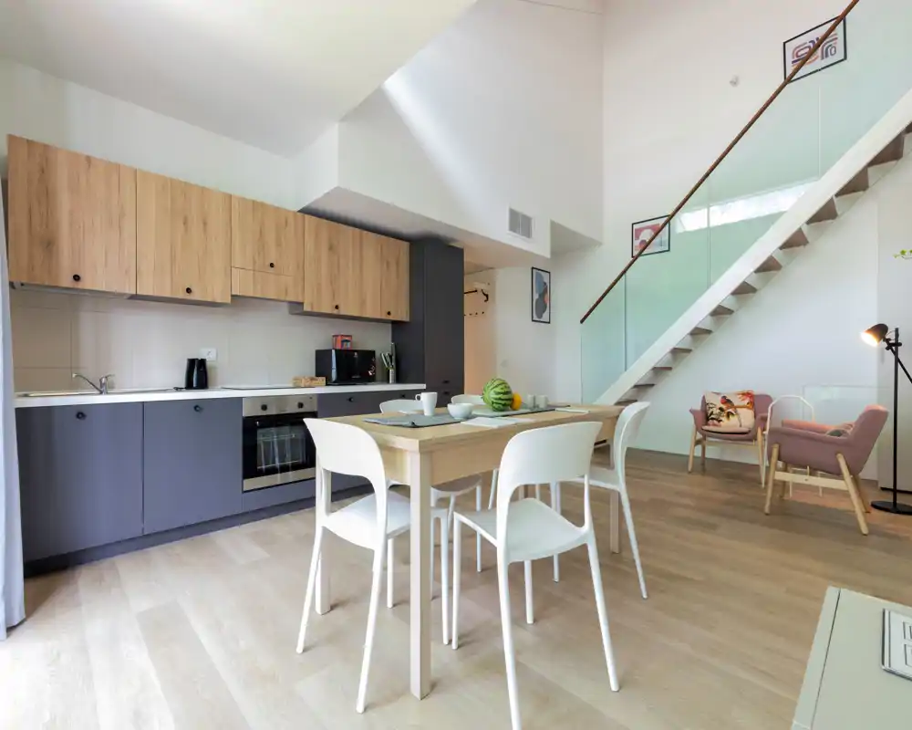 Modern open-plan kitchen with wood and grey cabinetry, integrated oven, and a dining table for four; bright, stylish and suitable for rental listings.