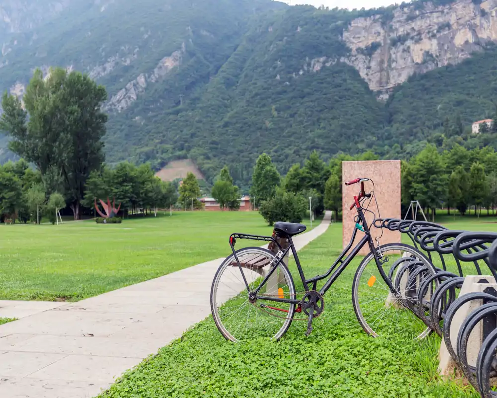 A parked bicycle next to a bike rack on a grassy park area with a paved path and a mountainous backdrop—ideal for outdoor listings highlighting green space and bike-friendly amenities.