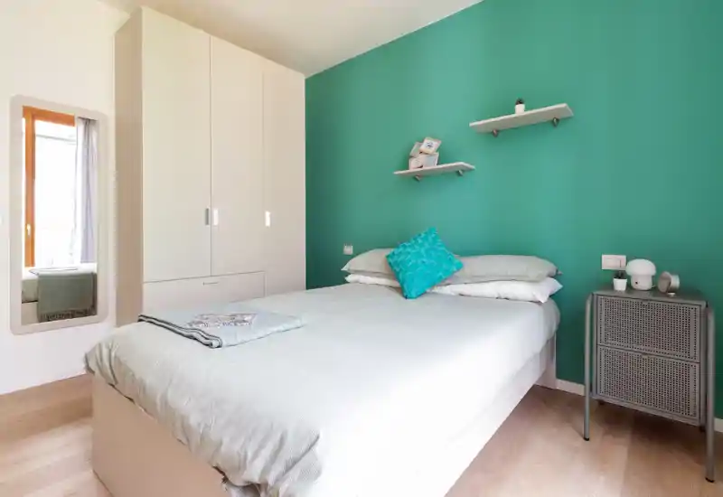 Bright, modern bedroom with a comfortable double bed, teal accent wall and a wardrobe. Natural light and clean styling make it ideal for rental listings.