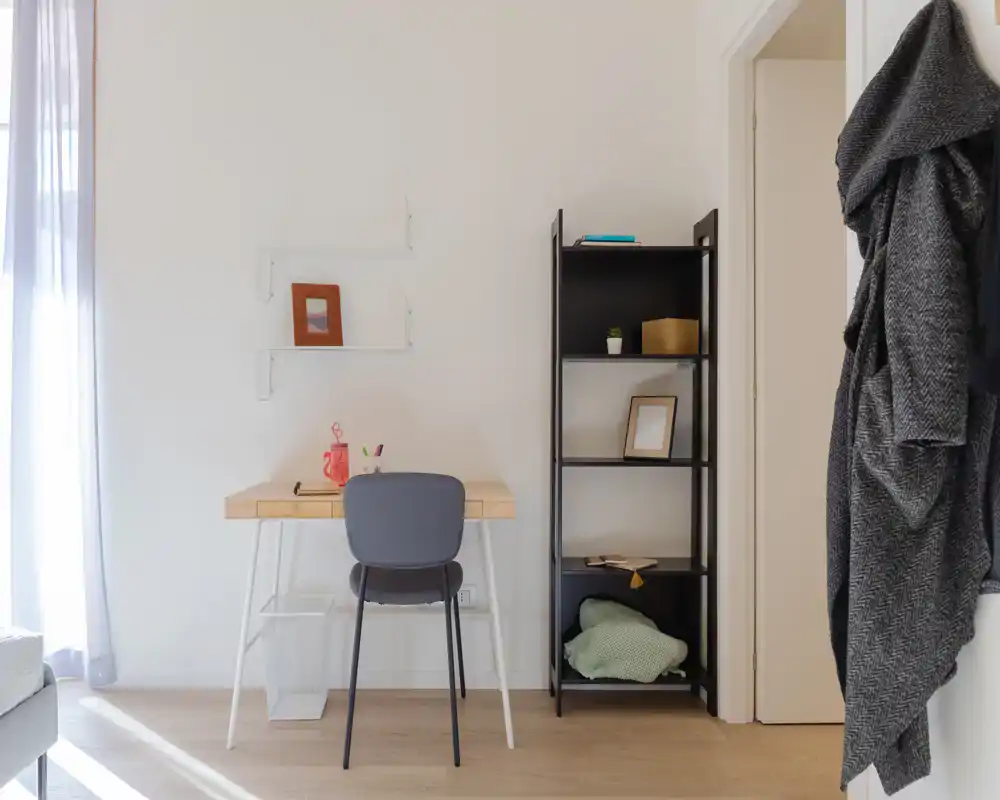 Angolo studio luminoso e minimale con scrivania, sedia e libreria, perfetto per lavorare in modo concentrato in un soggiorno compatto.