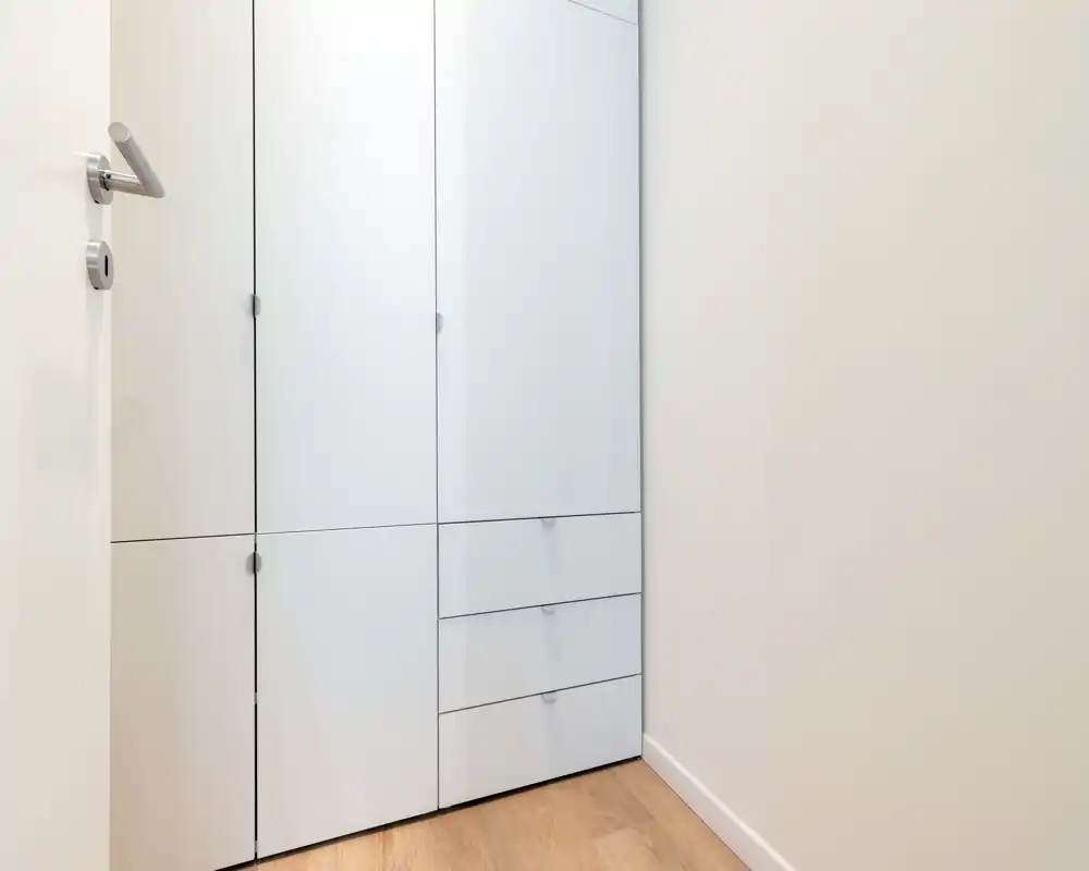 Piccolo ingresso/corridoio con armadi a muro bianchi e pavimento in legno chiaro, design minimale e pulito.