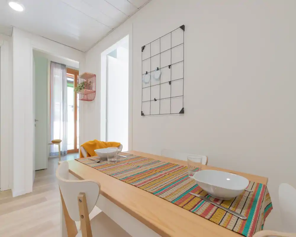 Coin repas moderne et lumineux avec table en bois dressée pour deux, chemin de table coloré et chaises contemporaines — idéal pour des repas décontractés.