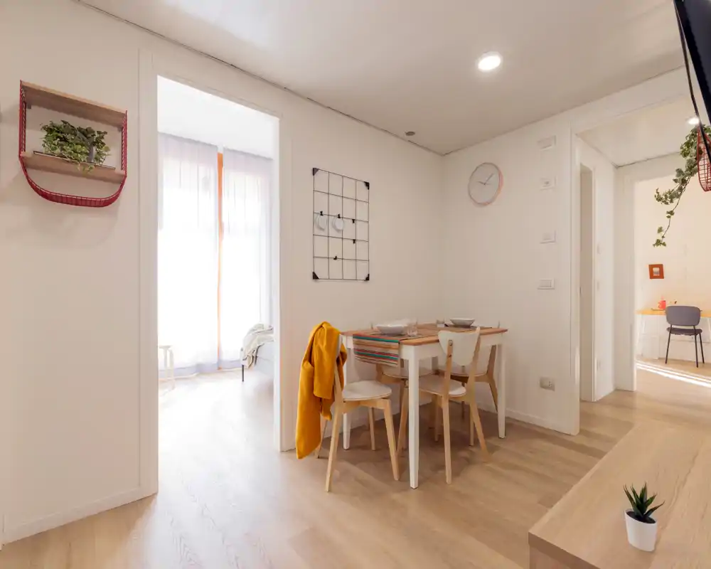 Coin repas lumineux et chaleureux avec table en bois et quatre chaises, déco chaleureuse et lumière naturelle venant des pièces adjacentes — idéal pour des repas conviviaux.