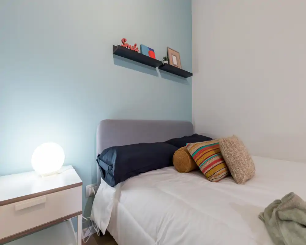 Dormitorio luminoso y bien arreglado con cabecero acolchado, cojines decorativos y una lámpara de mesa que aporta calidez.