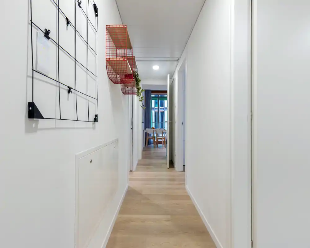 Long, bright hallway used as the entrance corridor with light wood floors, white walls and simple wall-mounted organizers leading toward the dining area.