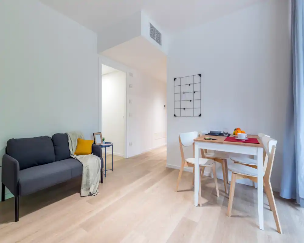Bright, modern living area with a compact sofa, small side table and a simple dining set — ideal for a cozy two-person apartment.