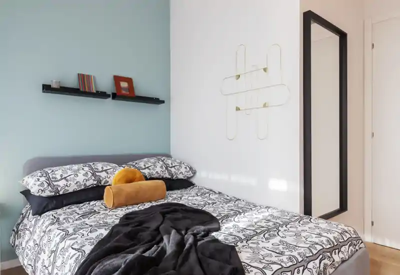 Bright, stylish bedroom with a patterned bedspread, decorative pillows and natural light; clean modern accents and wall decor create a cozy atmosphere ideal for rental photos.