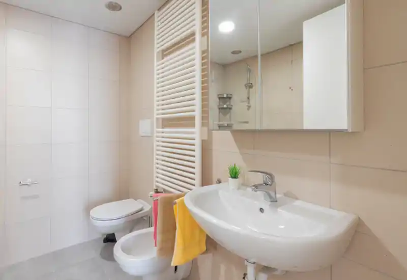 Clean, modern bathroom with a wall-mounted toilet, bidet, sink and mirrored cabinet. Neutral tiles and bright lighting make the room feel fresh and well maintained.