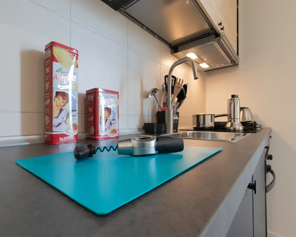 Angolo cucina moderno in primo piano con piano di lavoro pulito, lavello, piano cottura e utensili; lattine decorative e accessori danno un tocco casalingo.