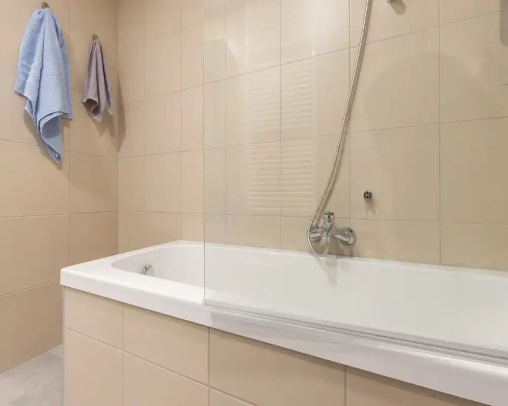 Bagno moderno e luminoso con vasca piastrellata, doccia a parete, piastrelle beige neutre e due asciugamani appesi.