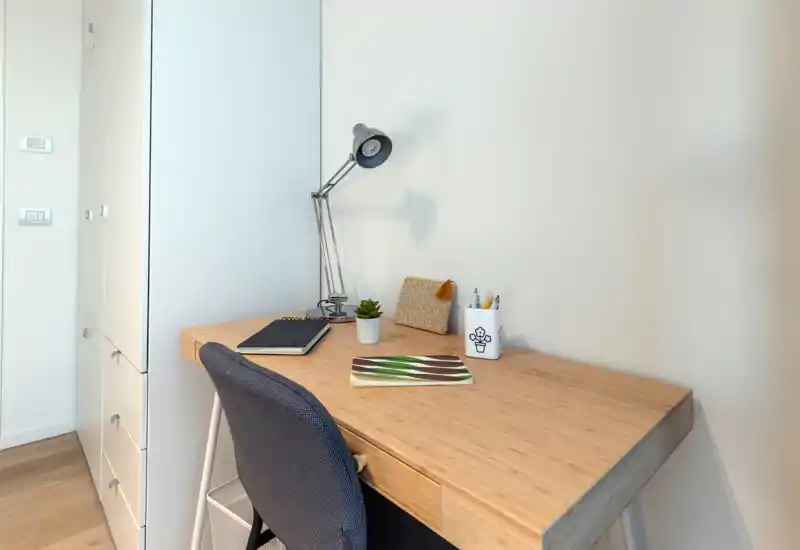 Rincón de oficina en casa luminoso y minimalista con escritorio de madera, lámpara de trabajo, cuaderno y una silla tapizada cómoda — ideal para trabajar o estudiar.