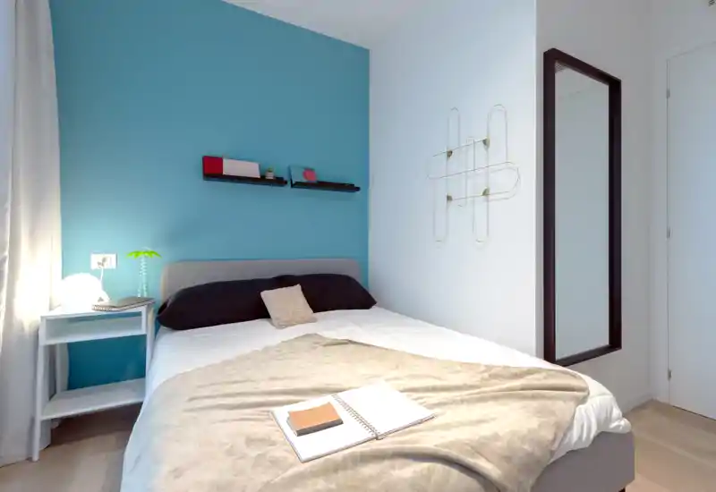 Dormitorio luminoso y moderno con pared de acento turquesa, cama doble cómoda, mesita de noche y ropa de cama suave, ideal para un anuncio de alquiler acogedor.