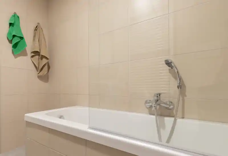 Baño moderno y limpio con bañera alicatada, grifo empotrado con ducha de mano y dos toallas colgadas.