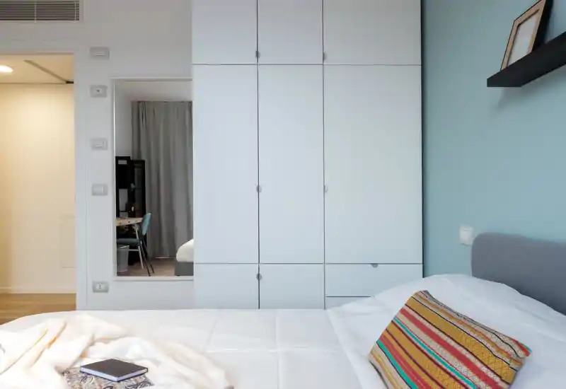 Dormitorio moderno y luminoso con una cama grande en primer plano, pared azul clara y un gran armario blanco; textiles acogedores y estilo ordenado.