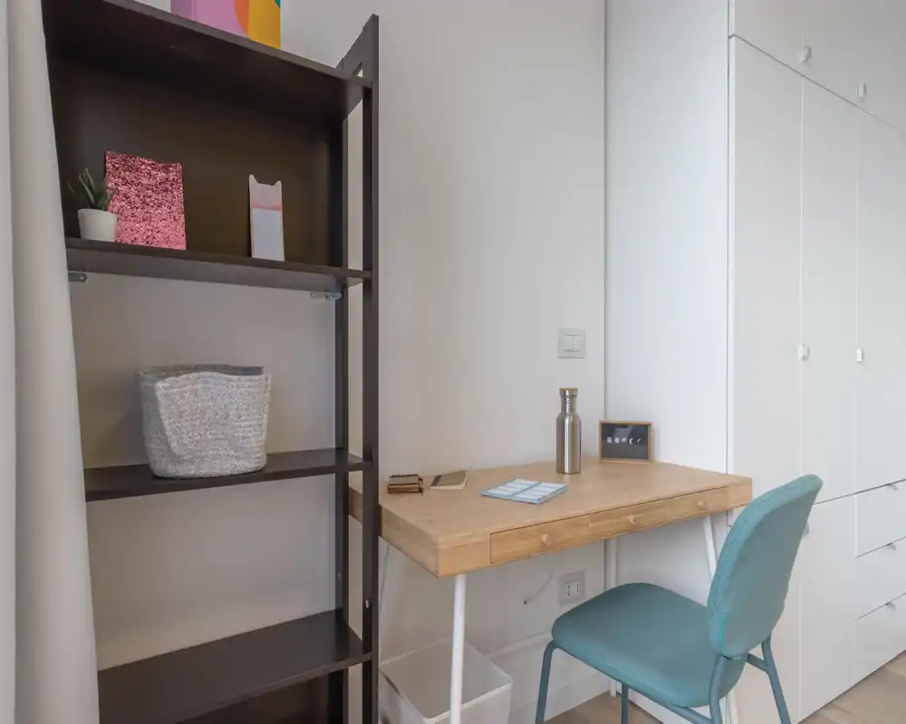 Compact, tidy workspace with a wooden desk, teal chair and open shelving — ideal for a quiet home office corner.