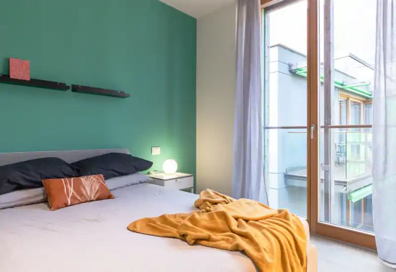 Bright, modern bedroom with a large bed, warm textiles and a floor-to-ceiling window that fills the room with natural light.