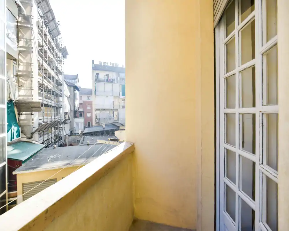 Pequeño balcón soleado con vistas a edificios vecinos, barandilla baja y puerta acristalada que da al interior — ideal para un espacio exterior compacto.