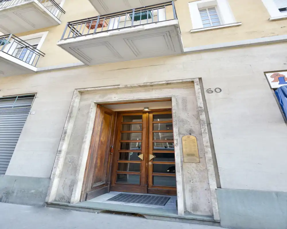 Entrada a pie de calle con puerta doble de madera enmarcada en piedra, felpudo y un interfono/placa junto a la puerta.