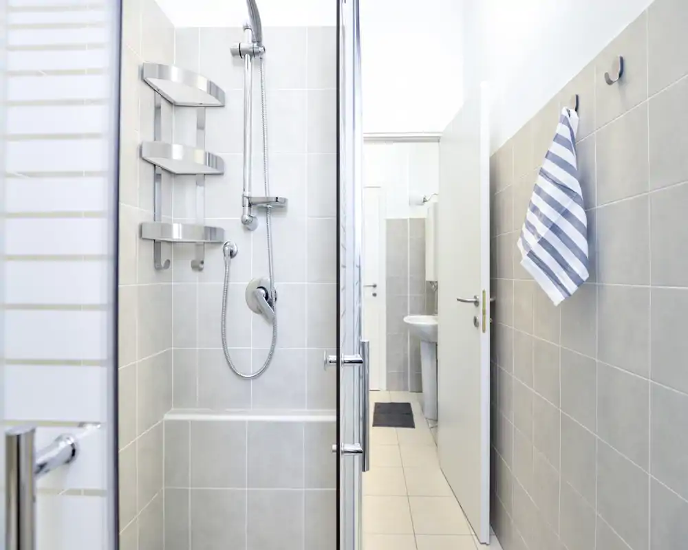 Cuarto de baño moderno y luminoso con ducha alicatada, cabezal de ducha empotrado y grifería cromada; una toalla a rayas cuelga en la pared y se ve el lavabo por la puerta abierta.