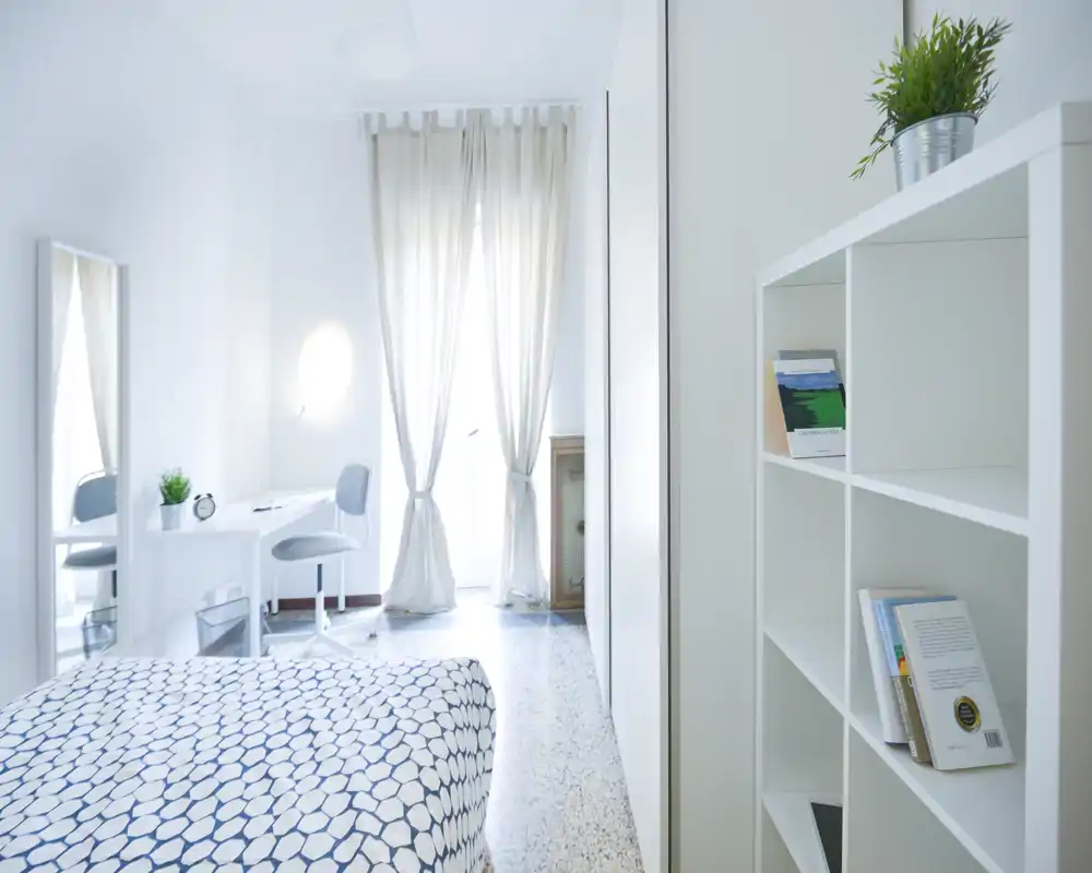 Chambre lumineuse et minimaliste avec couette à motifs, bureau près d'une fenêtre ensoleillée et étagères épurées — idéale pour des annonces recherchant une atmosphère fraîche et aérée.