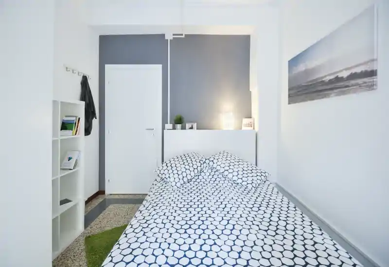 Chambre lumineuse et minimaliste avec lit à motifs, lampe de chevet, petites plantes et murs blancs épurés — idéale pour les locations de courte durée recherchant une atmosphère fraîche et aérée.