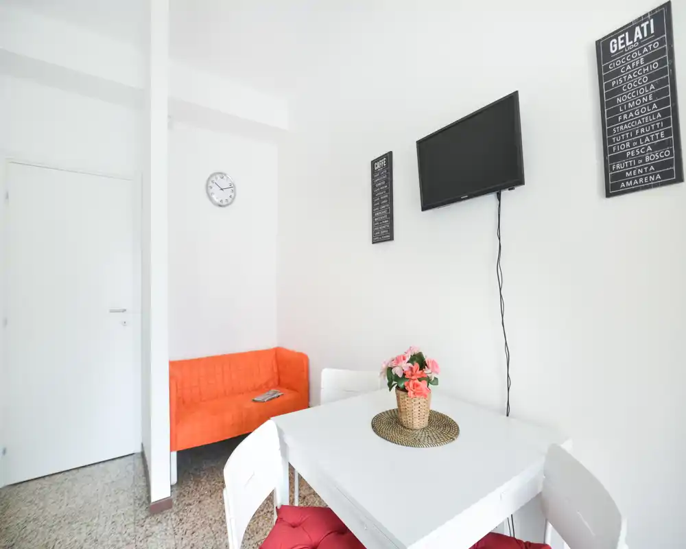 Espace de vie compact et lumineux avec un petit canapé orange, une TV murale et une table blanche décorée de fleurs — idéal pour un studio chaleureux.