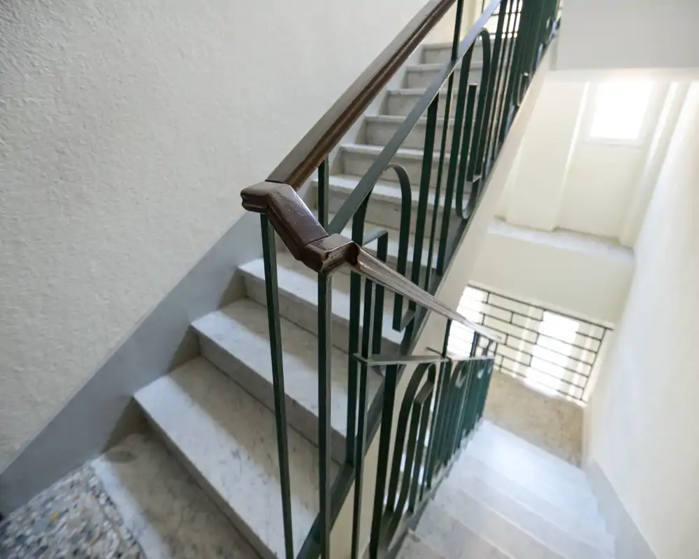 Cage d'escalier intérieure bien éclairée avec marches en marbre et rampe métallique décorative, idéale pour présenter les accès et zones de circulation.