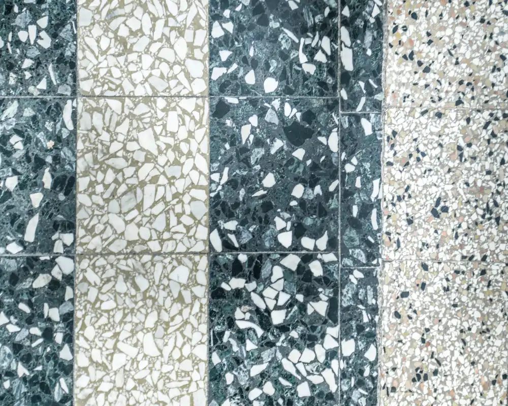 Gros plan d'un sol en terrazzo/galets avec trois bandes verticales présentant différents motifs de fragments de pierre ; aucun contexte de pièce visible.