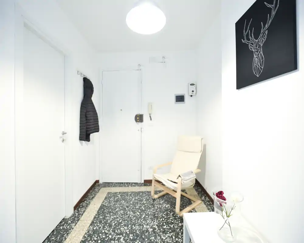 Entrée lumineuse et minimale avec un manteau accroché, un fauteuil léger et un sol carrelé moderne — propre et accueillante.