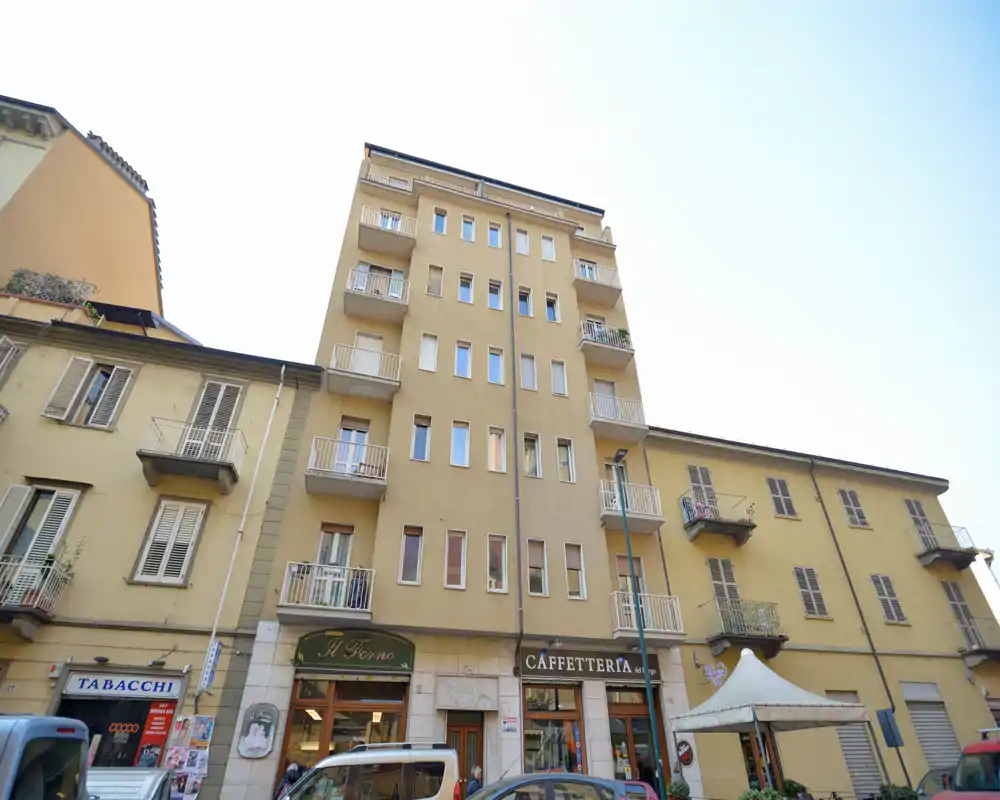 Vue extérieure d'un immeuble résidentiel à plusieurs étages avec commerces au rez-de-chaussée et balcons le long d'une rue; appropriée comme photo de façade ou de quartier pour une annonce.