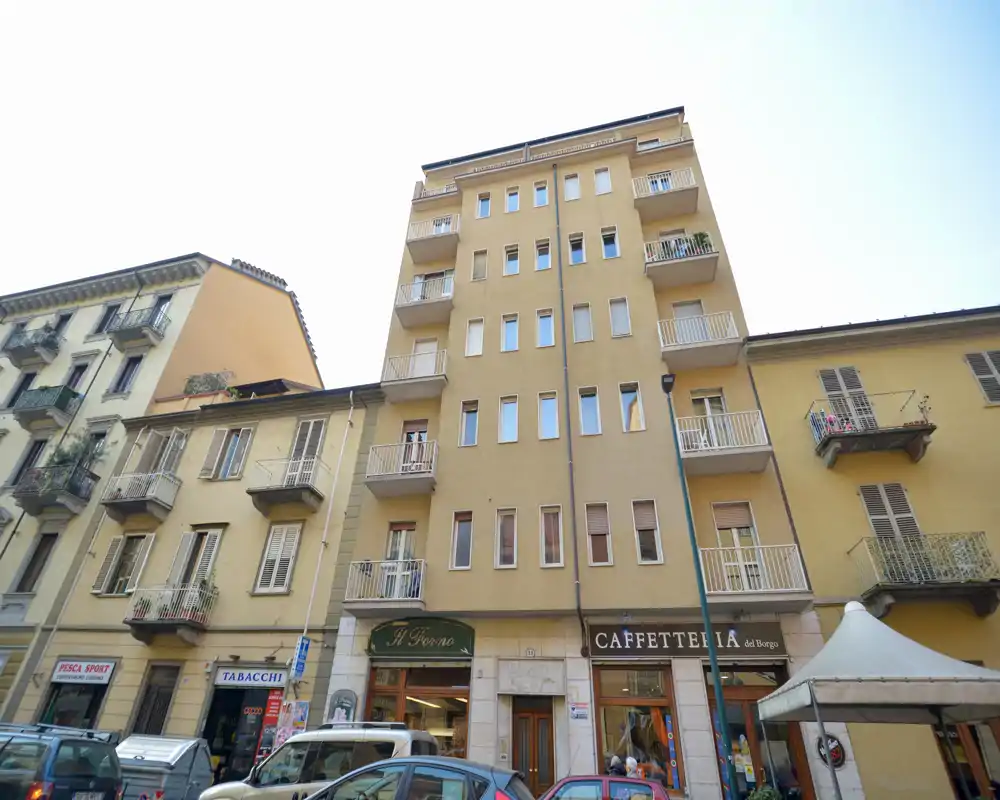 Façade d'immeuble donnant sur la rue avec plusieurs étages, balcons et commerces au rez-de-chaussée, dont une caffetteria — vue nette en pleine journée.
