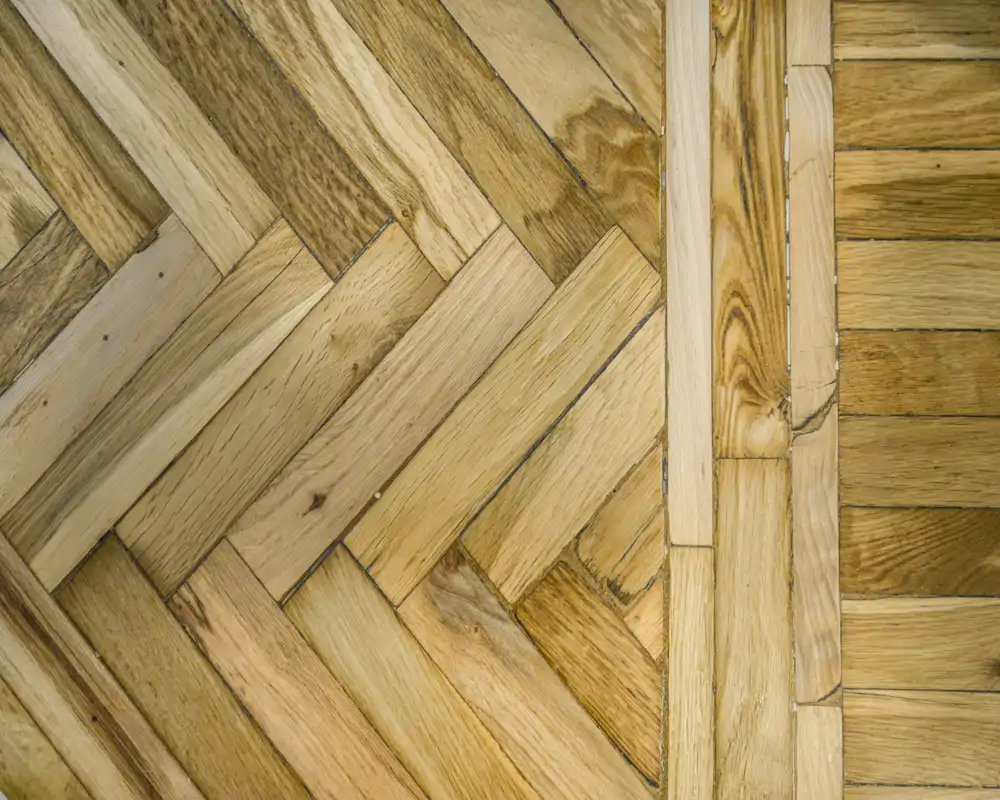 Gros plan d'un parquet en bois montrant des motifs en chevron et en lames droites ; aucun contexte de pièce visible.