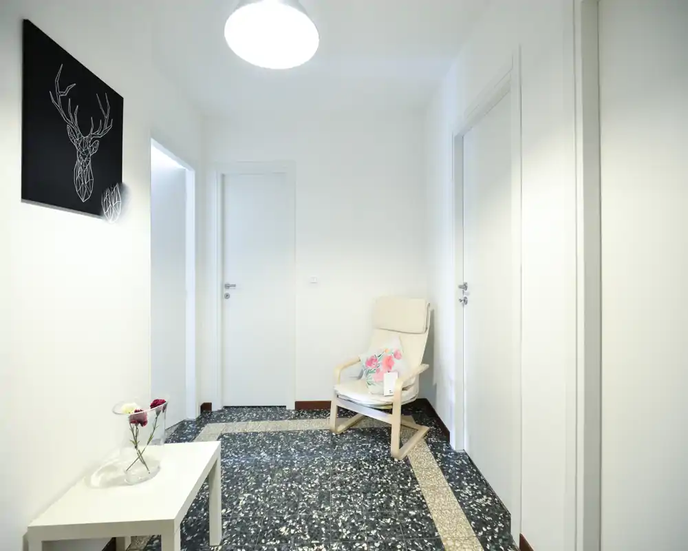 Entrée lumineuse et minimaliste avec un fauteuil clair, une petite table avec un vase et trois portes blanches — décoration moderne et sol type terrazzo.