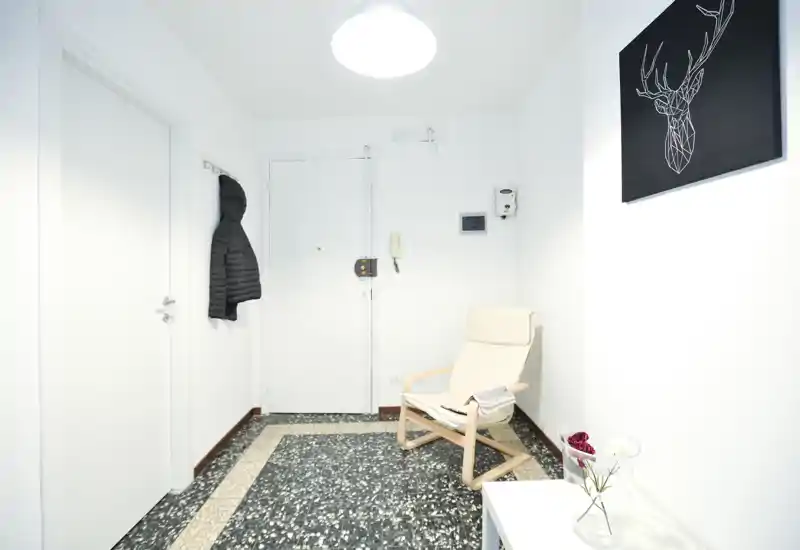 Ingresso luminoso e minimal con giacca appesa, una poltrona leggera e pavimento piastrellato moderno — pulito e accogliente.