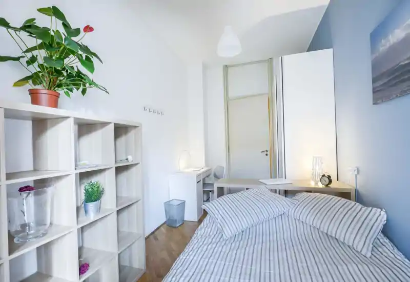 Bright, modern bedroom with a striped double bed, bedside table and a small desk — minimalist décor with plants and soft lighting.