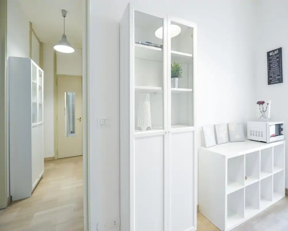 Bright, minimal living area corner with white storage units, decorative plant and wall art—clean Scandinavian-style styling ideal for a modern rental listing.