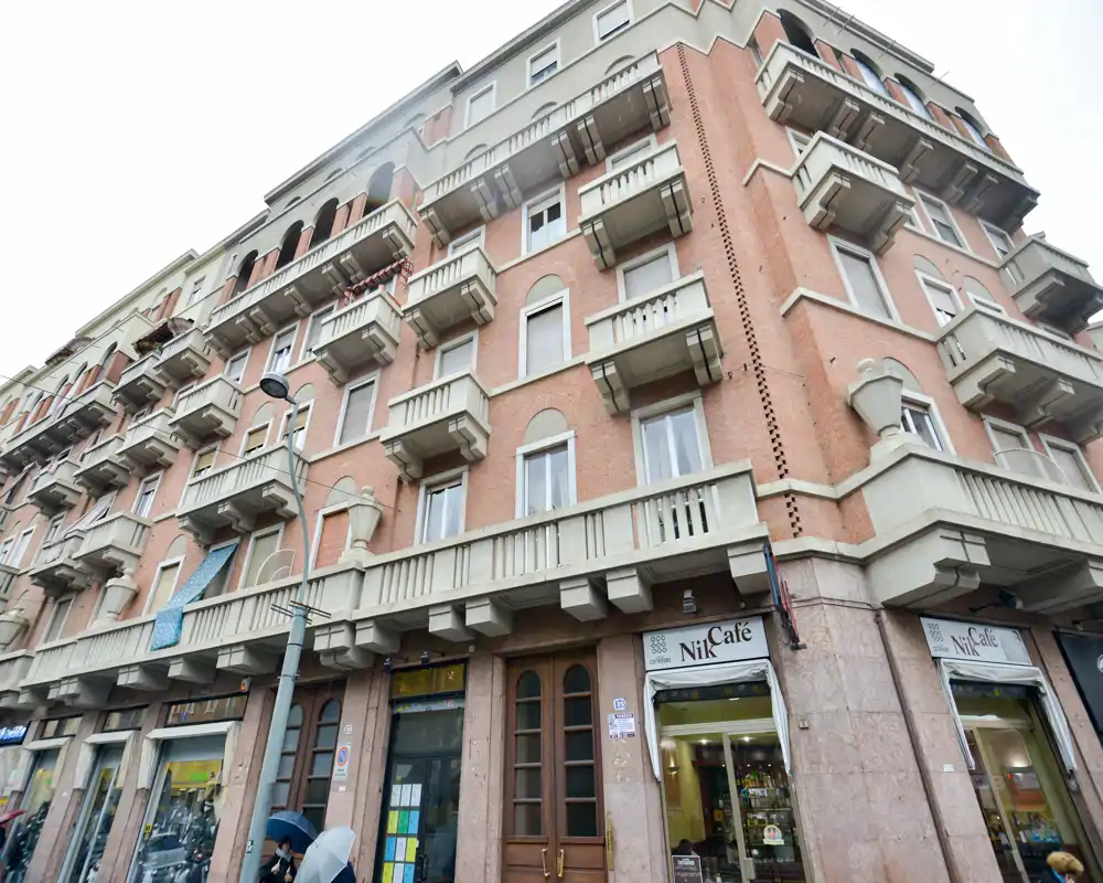Street-facing building facade with multiple small balconies and a ground-floor café; clear architectural details suitable for an exterior listing photo.