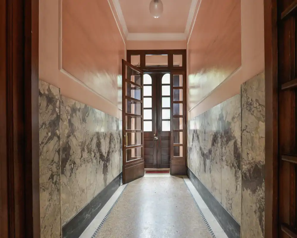 Spacious, symmetrical entrance hallway with decorative marble lower walls, wooden double doors and terrazzo floor — bright and well-preserved entry area ideal for welcoming guests.