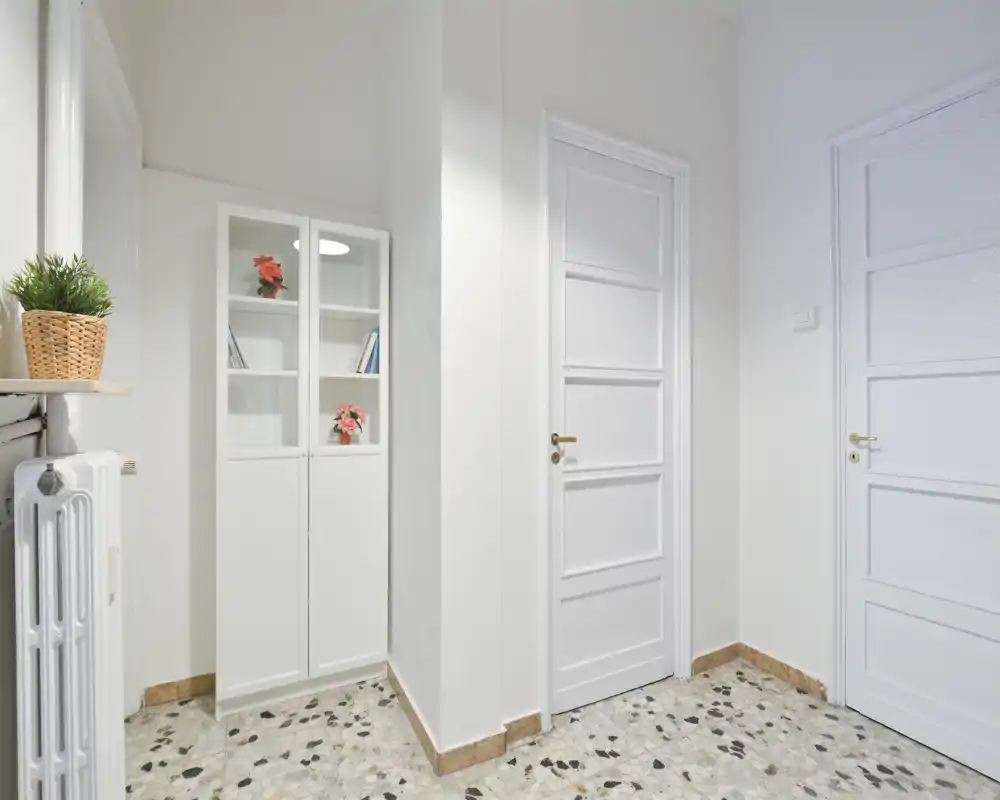 Bright, clean entrance hallway with white doors, a slim mirrored cabinet and decorative plants; terrazzo flooring and neat finishes create a welcoming first impression.